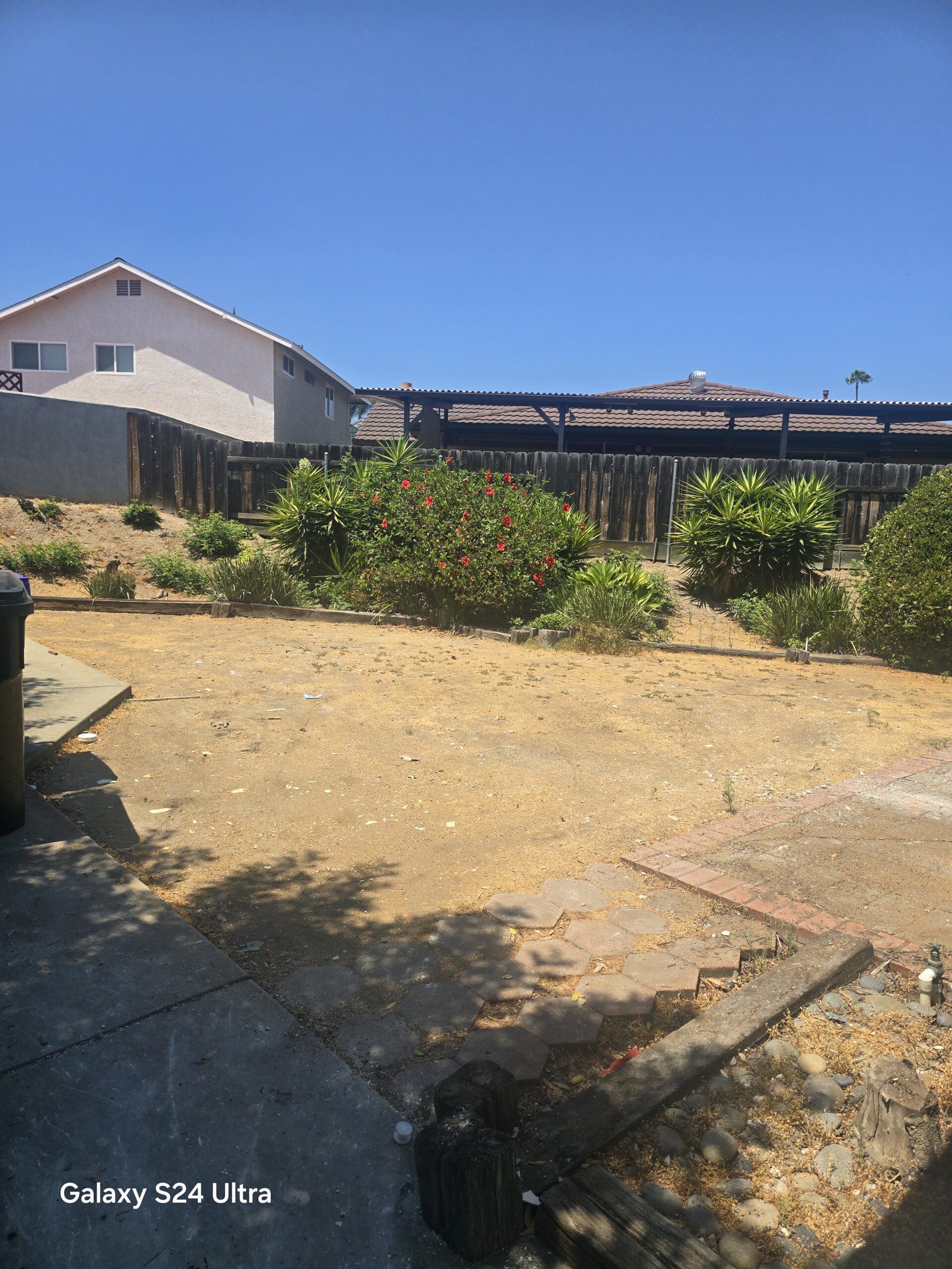 A dirt yard with a fence and a building in the background